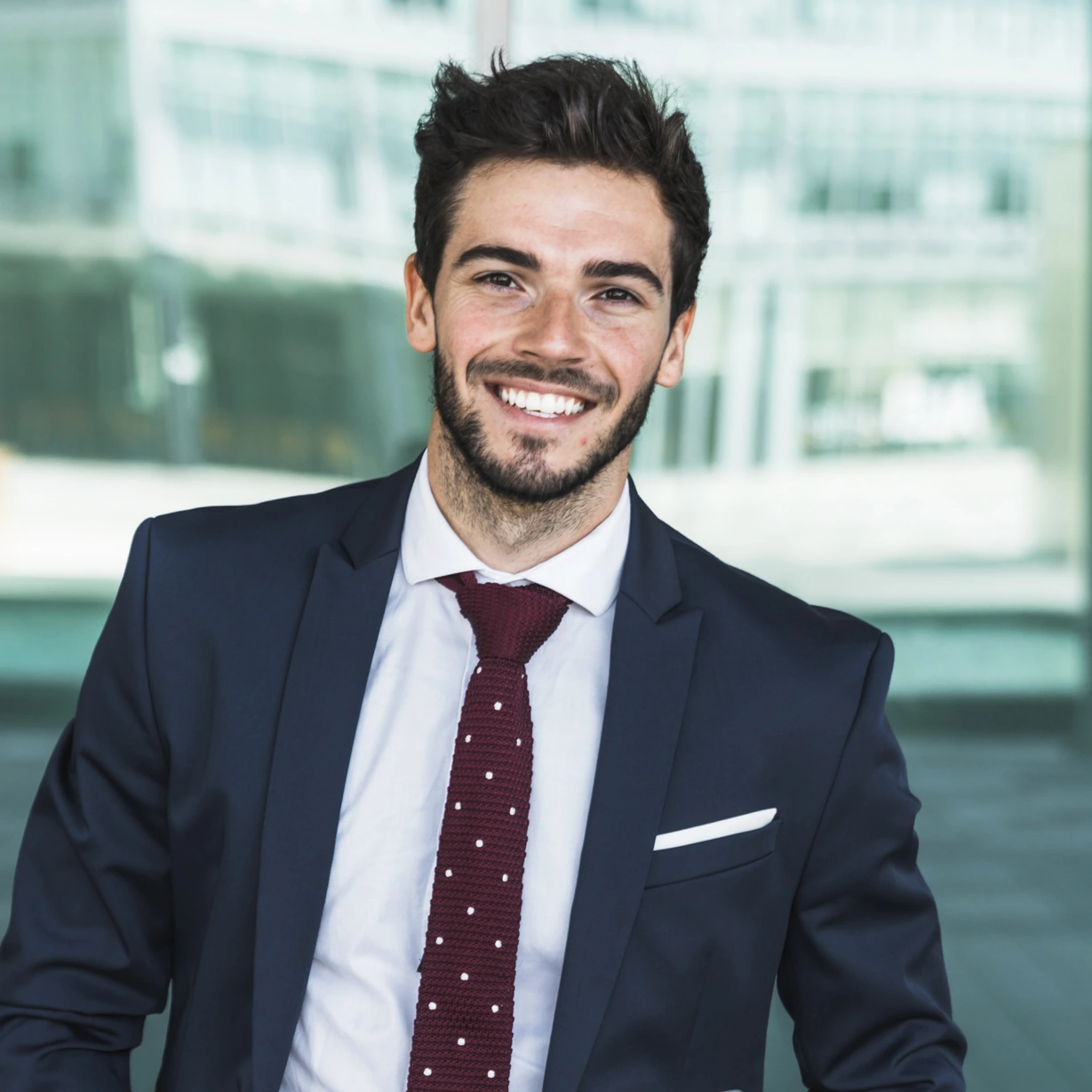 MBA Immobilienmanagement – angepasster Porträtausschnitt Mann im dunkelblauen Anzug mit Laptop vor einer Glasfassade.